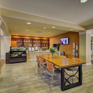 A modern cafe with a seating area featuring a long table, chairs, and a television on the wall.