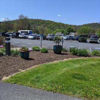 A view of a parking lot surrounded by landscaped flower beds and green grass, with mountains in the background under a clear blue sky.