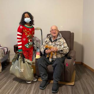 A joyful moment shared between a young girl in festive clothing and an elderly man, both smiling together during the holiday season.