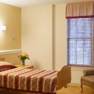 A cozy bedroom with a single bed, armchair, and window with patterned curtains.