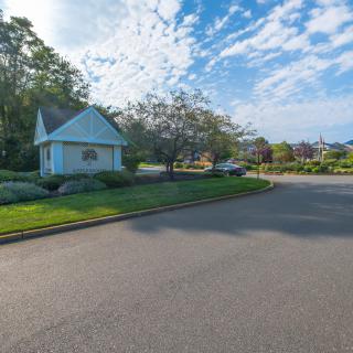 A suburban street with a small house, trees, and a clear blue sky.
