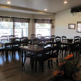 A cozy dining area featuring wooden tables and chairs, illuminated by natural light from large windows.