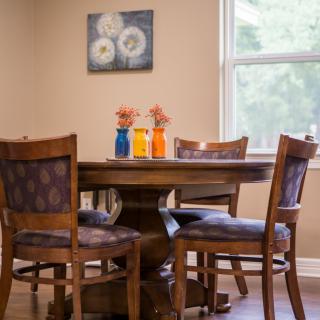 A cozy dining area with a wooden table, surrounded by four chairs and decorated with colorful vases of flowers.