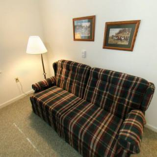 A cozy living room corner featuring a plaid couch, standing lamp, and framed pictures on the wall.