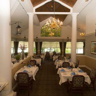 An elegant restaurant interior with neatly arranged tables and chairs, highlighted by a chandelier.
