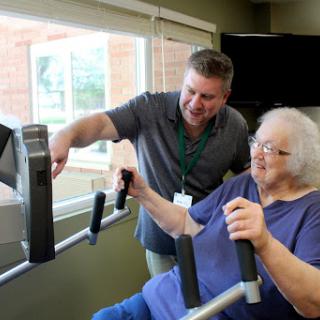 A trainer assists an elderly woman during a fitness session, focusing on rehabilitation and exercise.