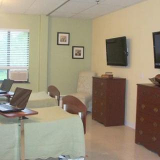 A cozy room with two beds, chairs, and televisions on the wall.