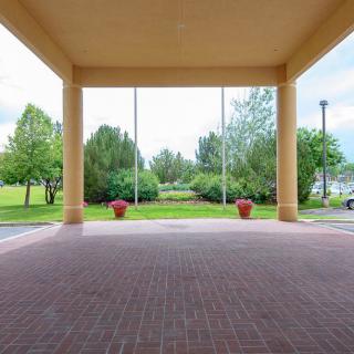 A covered walkway with brick flooring opens to a scenic outdoor view with trees and planters.