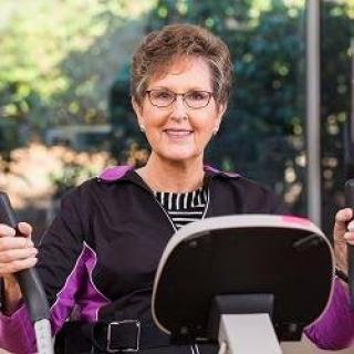 An elderly woman exercises on gym equipment, showcasing an active lifestyle.