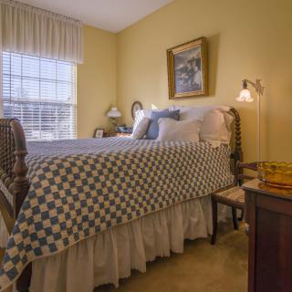 A cozy bedroom featuring a neatly made bed with patterned bedding, soft lighting, and traditional decor elements.