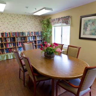 A cozy meeting room with a large wooden table surrounded by chairs, flanked by bookshelves and decorated with indoor plants.