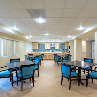 A spacious dining area with multiple tables and chairs, featuring an adjacent kitchen.