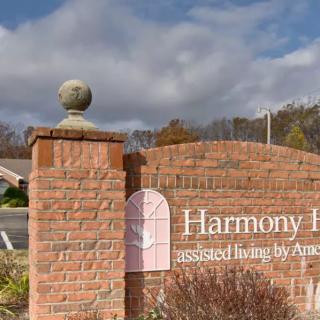 A brick sign with 'Harmony Hill' inscribed, set against a cloudy sky backdrop.