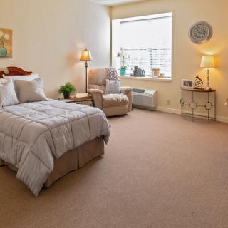 A cozy bedroom with a neatly made bed, armchair, and soft lighting.