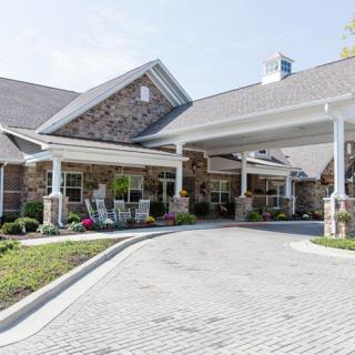 A welcoming entrance to a stone building with a covered driveway and landscaped surroundings.