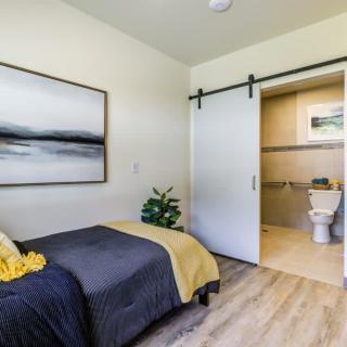 A modern and minimalist bedroom featuring a sliding door leading to an en-suite bathroom.
