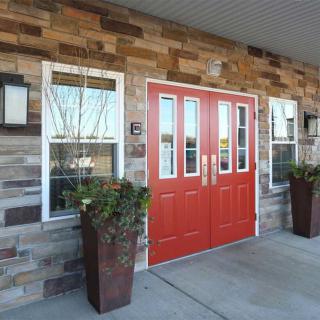 A building entrance featuring a bright red double door set in a stone wall, with potted plants and windows on either side.
