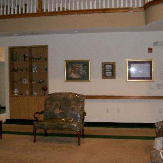 A cozy living room interior featuring a sofa, artwork on the walls, and a shelf with decorative items.