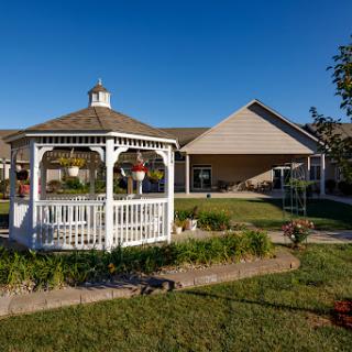 A serene outdoor space featuring a white gazebo surrounded by lush greenery and a clear blue sky.