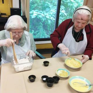 Two elderly women engaged in a cooking activity, preparing ingredients at a table.