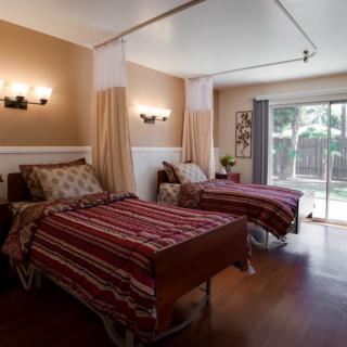 A warmly lit shared room in a nursing home featuring two beds separated by curtains.