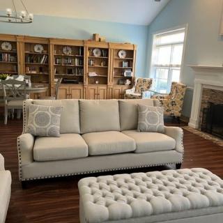 A cozy living room with a beige sofa, tufted ottoman, and wooden bookshelves along one wall.