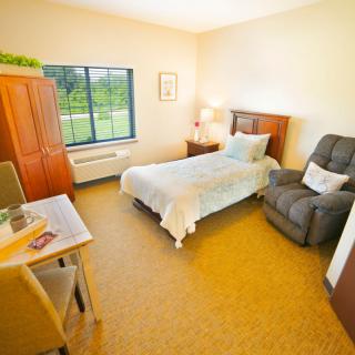 A cozy bedroom with a single bed, armchair, and large window.