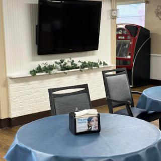 A cozy dining area featuring tables with blue tablecloths, a wall-mounted TV, and a vending machine in the background.