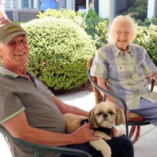 Two people sitting outdoors with a dog on a sunny day.