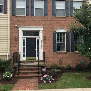 A brick house with a black front door, surrounded by well-maintained landscaping and flowers on either side of the entry steps.