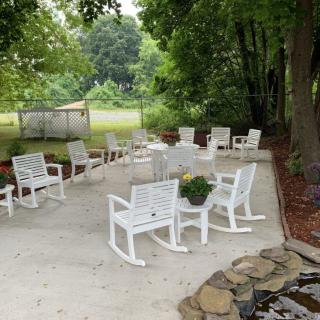 A serene outdoor patio area with white rocking chairs surrounded by greenery.