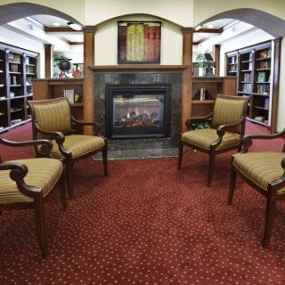 A cozy reading area in a library with chairs arranged around a fireplace.