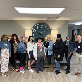 A group of people standing together in an office setting with a large clock on the wall.