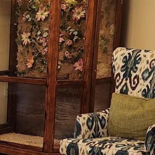 A cozy sitting area featuring a patterned armchair and a wooden cabinet with floral decorations.