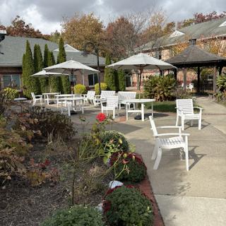 A serene outdoor patio area featuring white chairs and umbrellas surrounded by seasonal foliage.