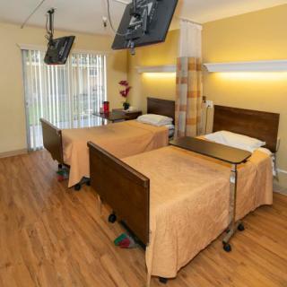 A hospital room with two medical beds, each equipped with a side table and overhead television.