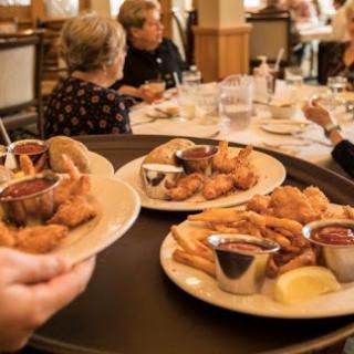 A server delivers plates of fried seafood to a dining table in a restaurant.