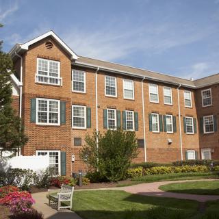 A three-story brick residential building with a small garden in the foreground under a clear blue sky.