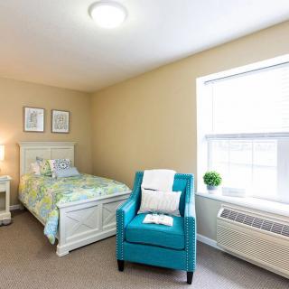 A cozy bedroom with a single bed and a turquoise armchair near a window.