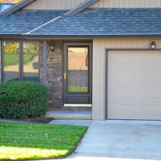 A charming house entrance featuring a well-maintained lawn and an attached garage.