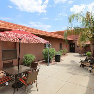 A sunny courtyard with outdoor seating and patio umbrellas, surrounded by a building and palm trees.