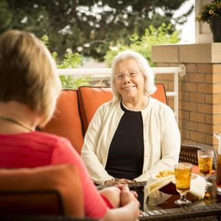 Two elderly women enjoying a conversation on a sunny patio.