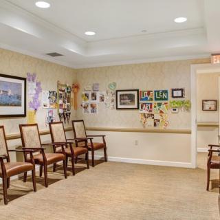 A cozy waiting room with chairs lined against the walls, decorated with colorful wall art and well-lit by ceiling lights.