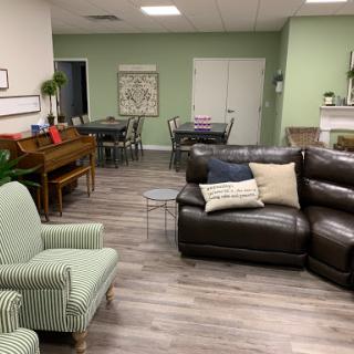A cozy living room and dining space featuring comfortable seating, a piano, and a warm color palette.