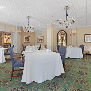 A spacious dining area with elegantly set tables, comfortable chairs, and decorative chandeliers.