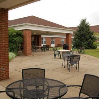 A peaceful outdoor patio area with tables and chairs adjacent to a brick building, surrounded by greenery.