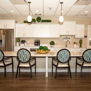 A modern kitchen with white cabinets, a large countertop, and stylish chairs.