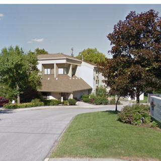 A residential building with trees and a driveway in the foreground.