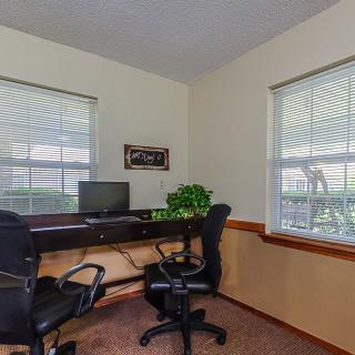 A small office space with a desk, computer, and chairs by two large windows.
