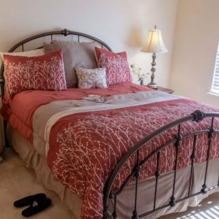 A cozy bedroom featuring a neatly made bed with patterned bedding and decorative pillows, accompanied by a lamp on the bedside table.